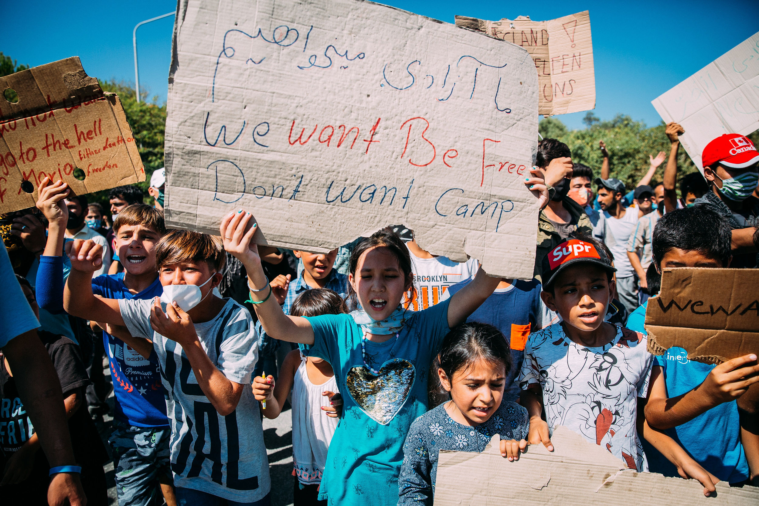Menschen protestieren, ein Kind hält ein Schild mit der Aufschrift "We want be free, dont want camo"