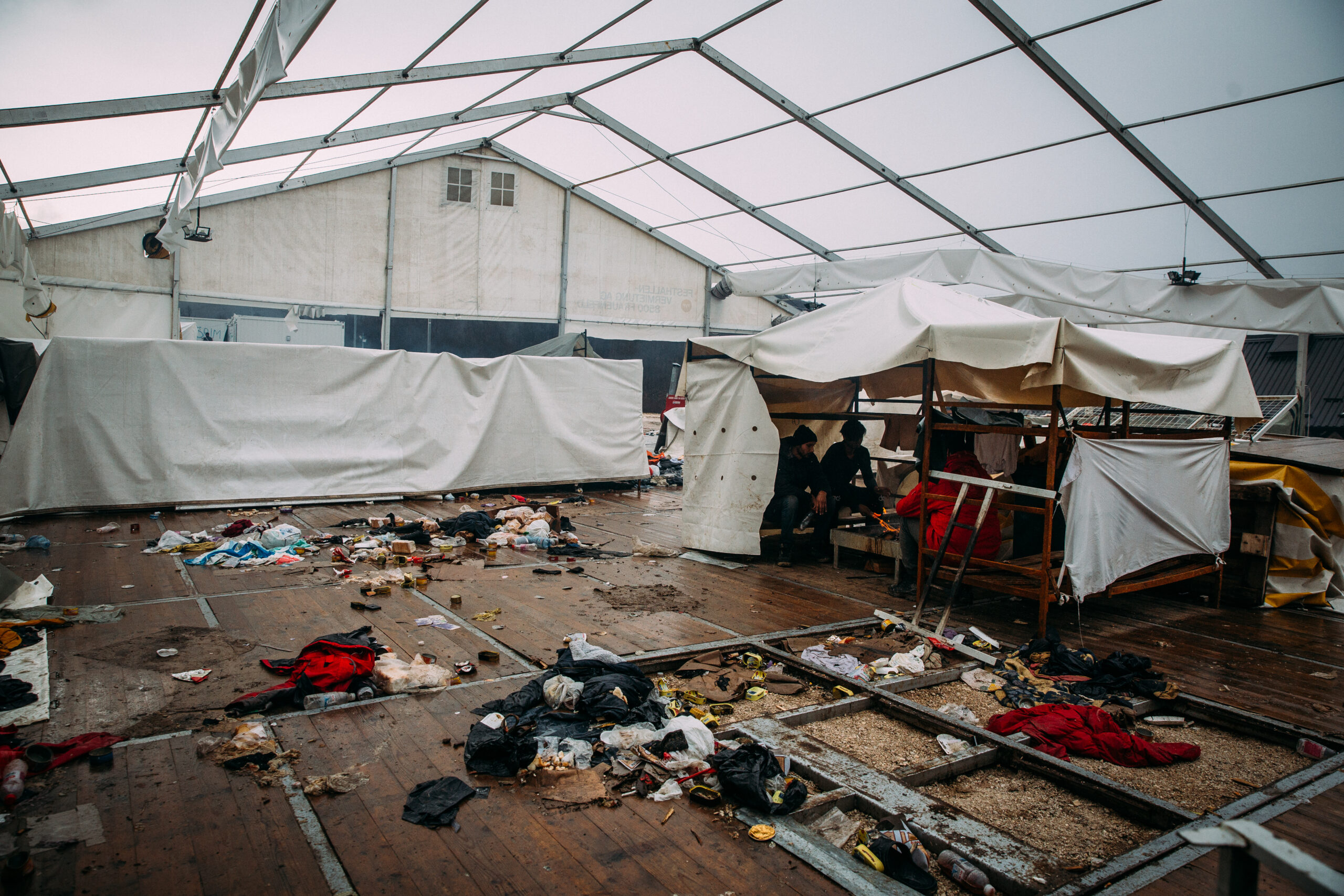 Kleine Zelte in einem Festzelt, auf dem Boden liegen Müll und andere Sachen